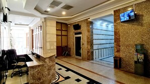 Un hall d’entrée avec un comptoir de réception, une colonne en marbre, une caméra de surveillance et un distributeur d’eau.