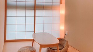Una stanza con un paravento scorrevole shoji, un tavolo di legno, un cuscino da pavimento intrecciato e un quadro appeso al muro.