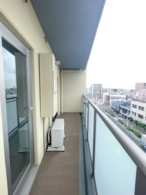 A balcony with a view of the city, a window with a metal screen, and a white cabinet. - Shinkou House UE (Osaka)
