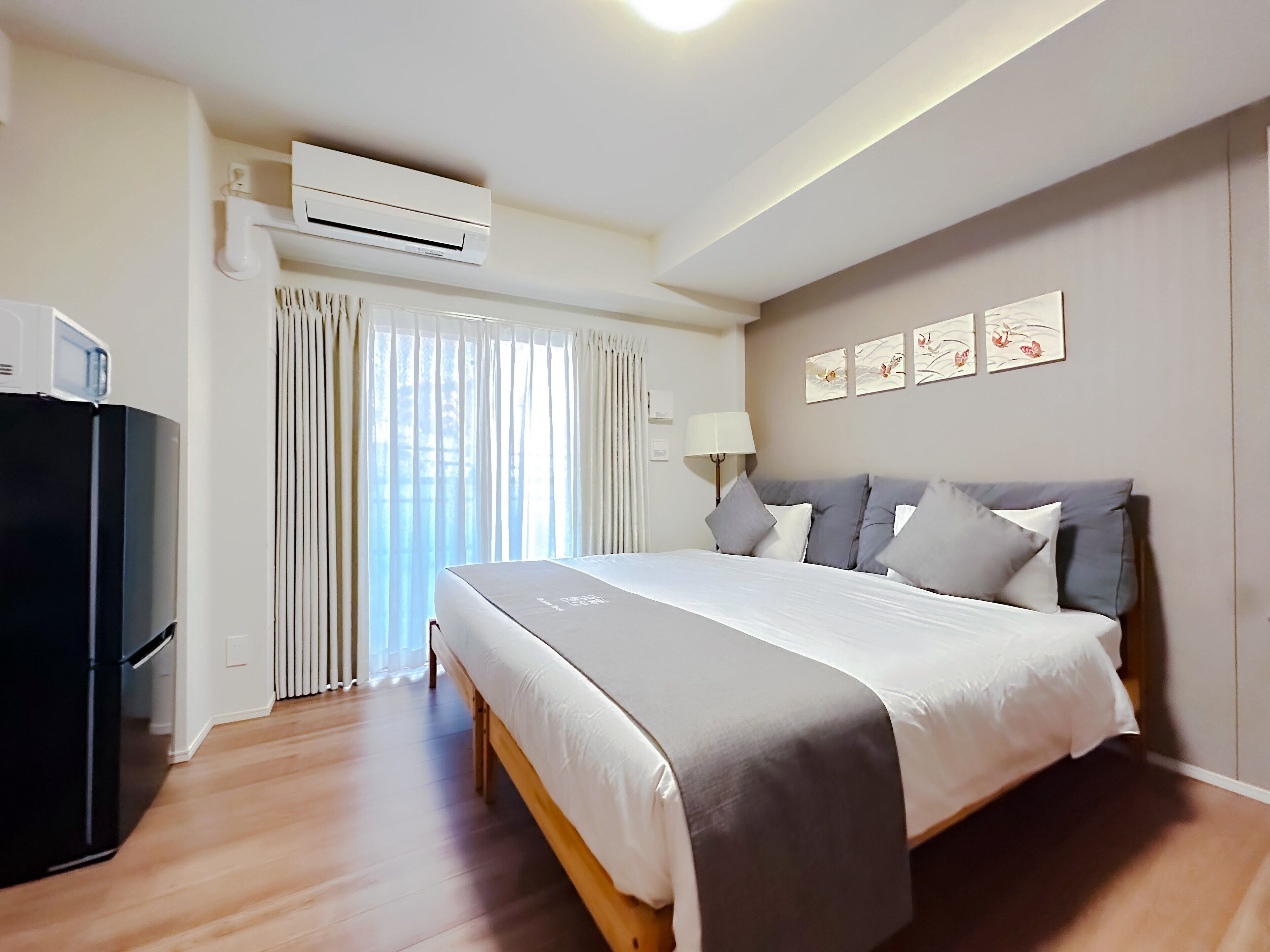 Habitación de hotel con cama, refrigerador, ventana con cortinas, aire acondicionado y decoración en la pared.