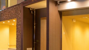 L'ingresso di un hotel con facciata in pietra, un cartello con la scritta "Shinko House Uehonmachi East" e una telecamera di sicurezza sopra la porta.