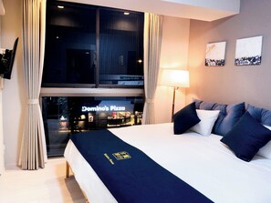 A hotel room with a bed, a window with curtains, a lamp, and artwork on the wall. - Shinkou House UE (Osaka)