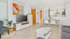 A modern living room with a flat-screen TV, a dining area with a table and chairs, and a kitchen with a clock on the wall. - Can Botana Casa 8 - By Dream Villas Pollensa (Cala San Vicente)