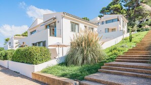 A modern two-story building with a flat roof, a balcony, and a staircase leading up to the entrance. - Can Botana Casa 8 - By Dream Villas Pollensa (Cala San Vicente)