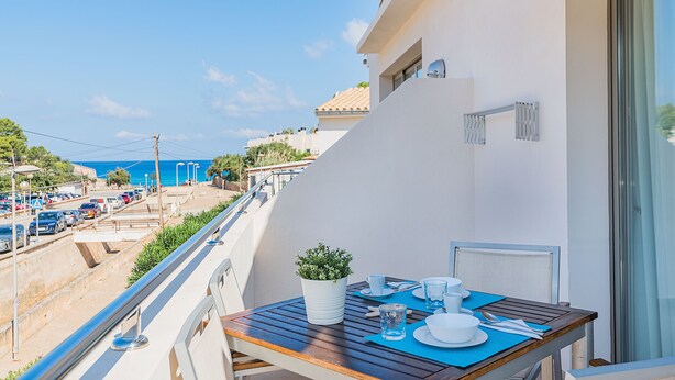 A balcony with a table set for two, overlooking a street and the sea. - Can Botana Casa 8 - By Dream Villas Pollensa (Cala San Vicente)