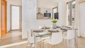 A modern dining area with a glass table, white chairs, and a clock on the wall. - Can Botana Casa 8 - By Dream Villas Pollensa (Cala San Vicente)