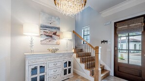 Un atrio con una scala in legno, un tavolo consolle bianco con lampade, un quadro raffigurante una barca e una porta con una finestra.