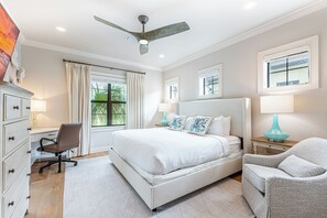 A bedroom with a large bed, a desk, a chair, and a ceiling fan.