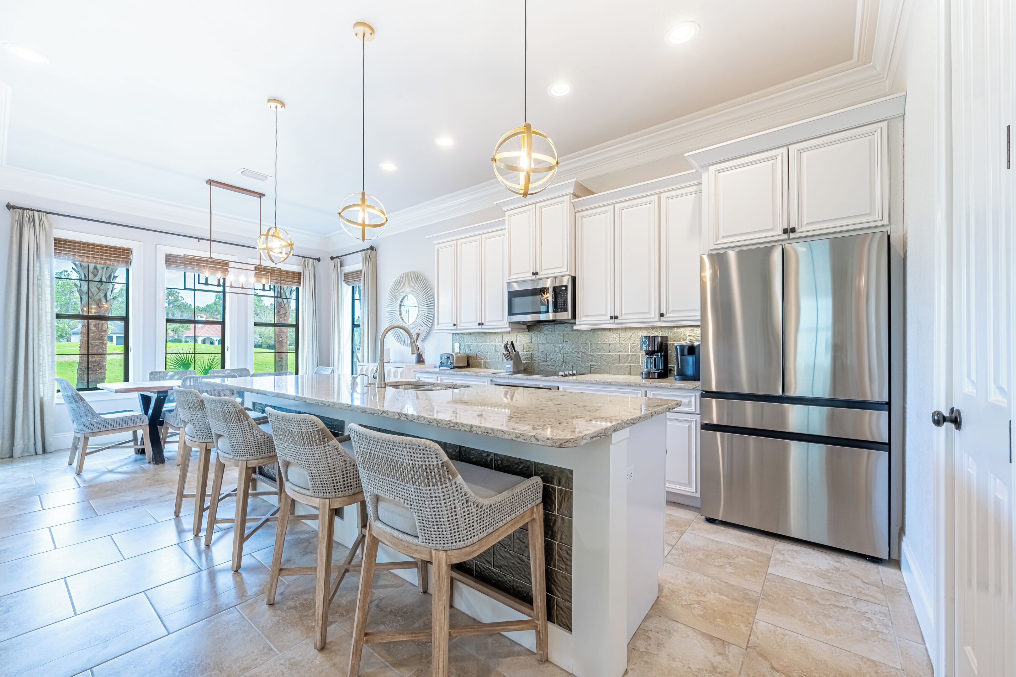 A modern kitchen with white cabinetry, a stainless steel refrigerator, a large island with bar stools, and pendant lighting.