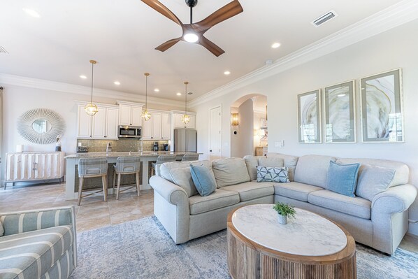 A spacious living area with a large sofa, a coffee table, and a dining area with a kitchen in the background.