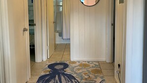 A hallway with white walls, a patterned rug, a hanging lamp, and a mirror. - Charming artist’s cottage near the beach, large lot with beautiful oaks (Oak Island)