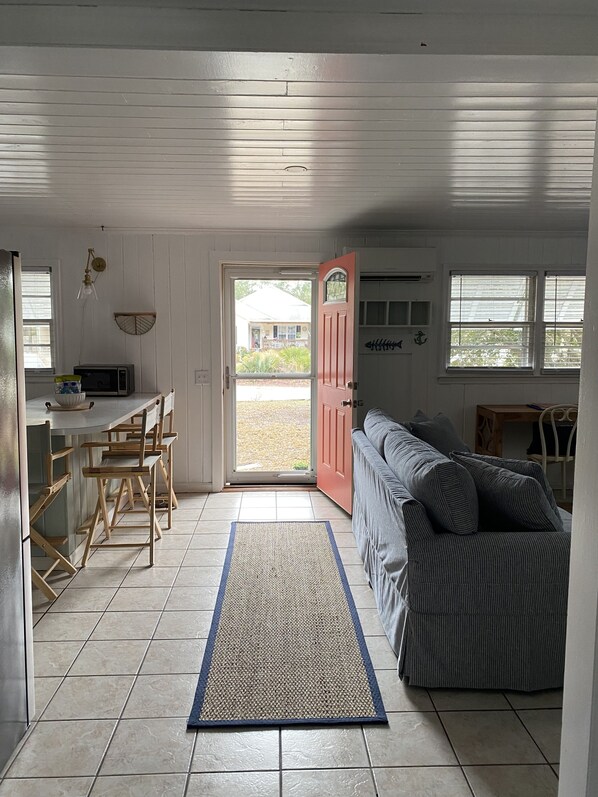 Un espace de vie compact comprenant un coin cuisine, un coin repas avec des chaises en bois, un canapé et une grande fenêtre.