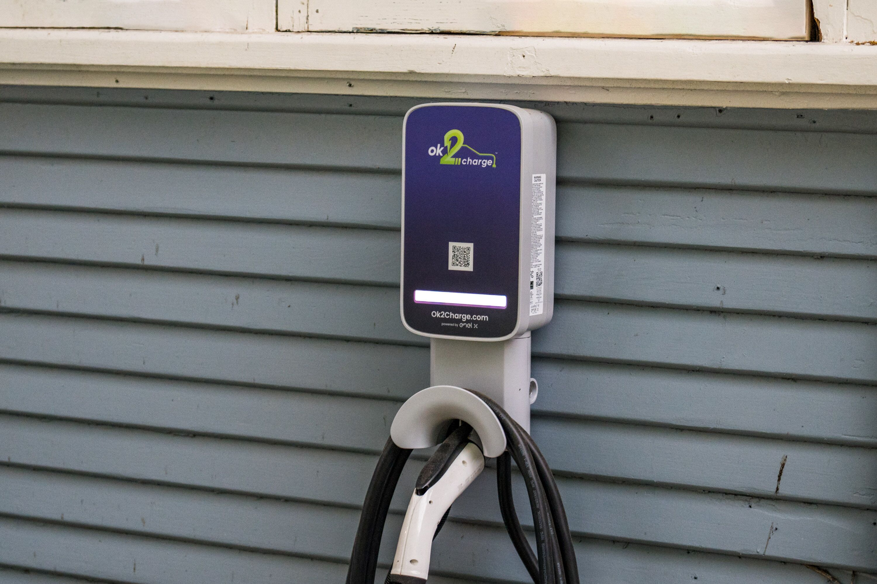 An electric vehicle charging station with a QR code and a website address.