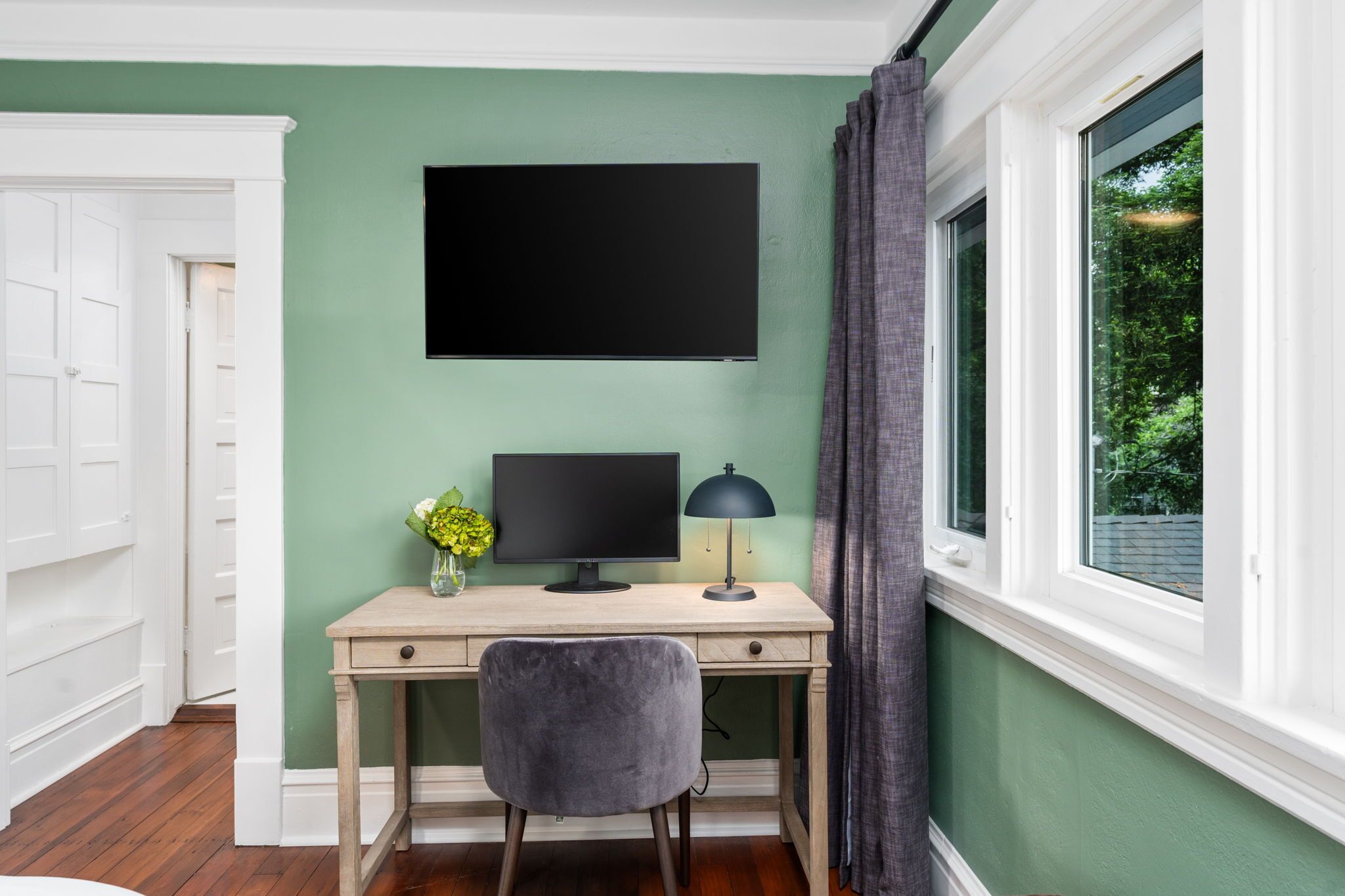 Una habitación con escritorio, televisión de pantalla plana, lámpara y ventana con cortinas.