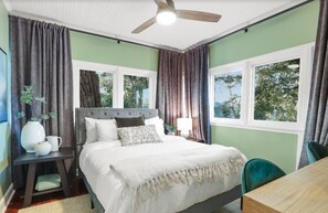 Un dormitorio con cama, mesita de noche, silla, mesa y ventilador de techo.