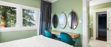 A bedroom with a bed, a desk with two chairs, and three wall mirrors.