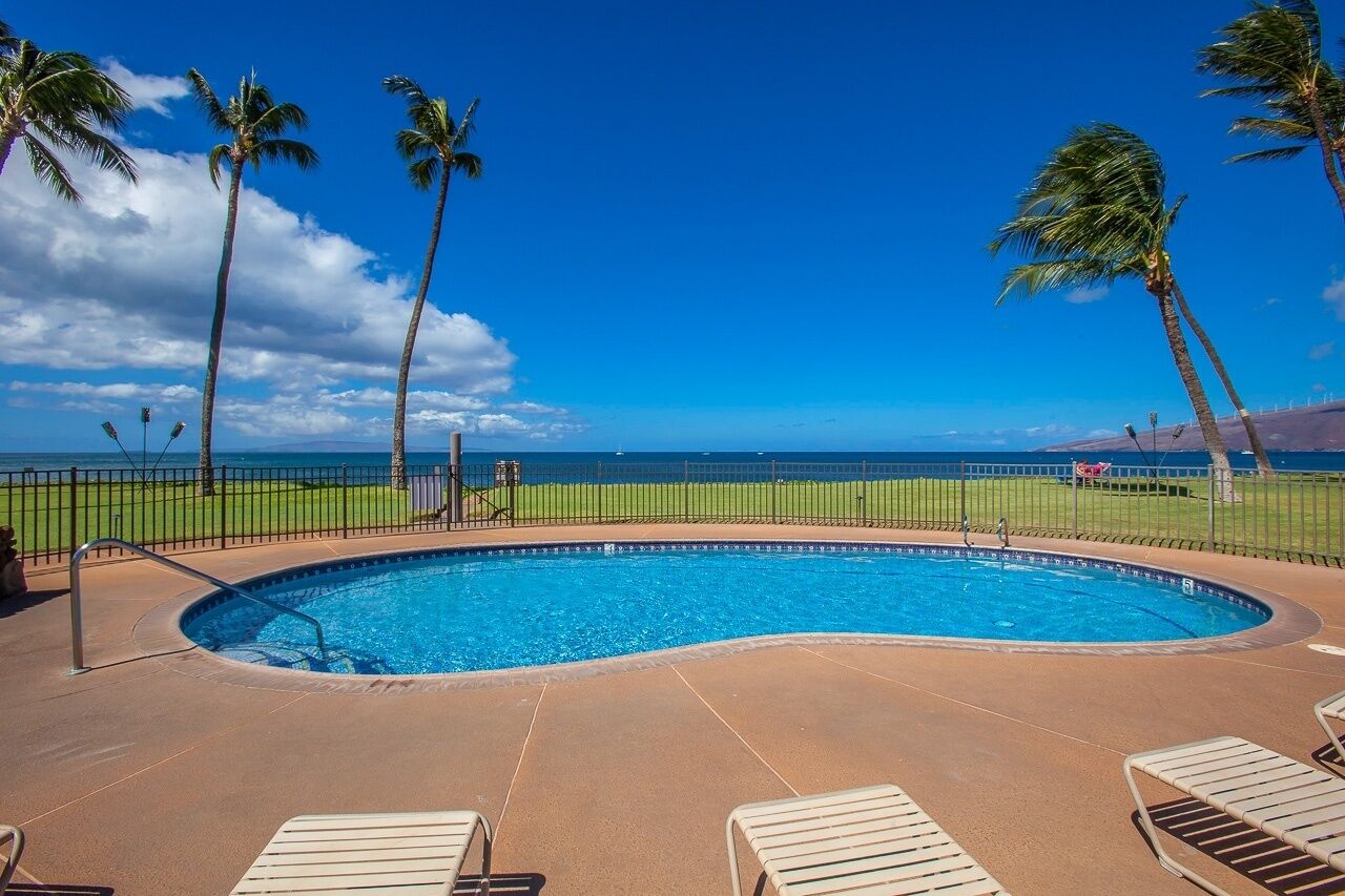 Piscina com vista para o oceano, rodeada por palmeiras e uma cerca.