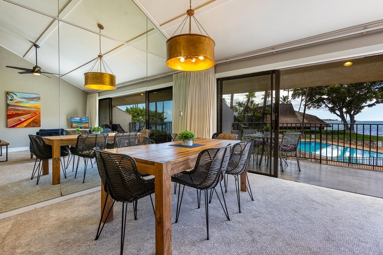 Un amplio comedor con una mesa de madera y sillas negras, con vistas a una piscina y al océano.