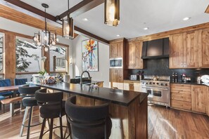 Une cuisine moderne avec des meubles en bois, un grand îlot central doté de tabourets de bar, des appareils électroménagers en acier inoxydable et une grande fenêtre offrant une vue sur la neige.
