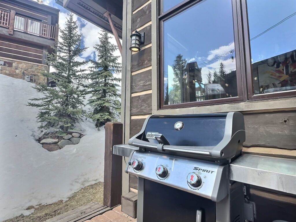 A Spirit gas grill with three burners, a stone wall, and a wooden building with a window.