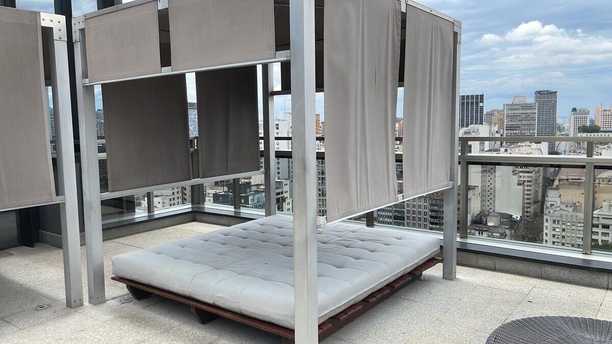 A balcony with a mattress and metal frame, overlooking a cityscape.