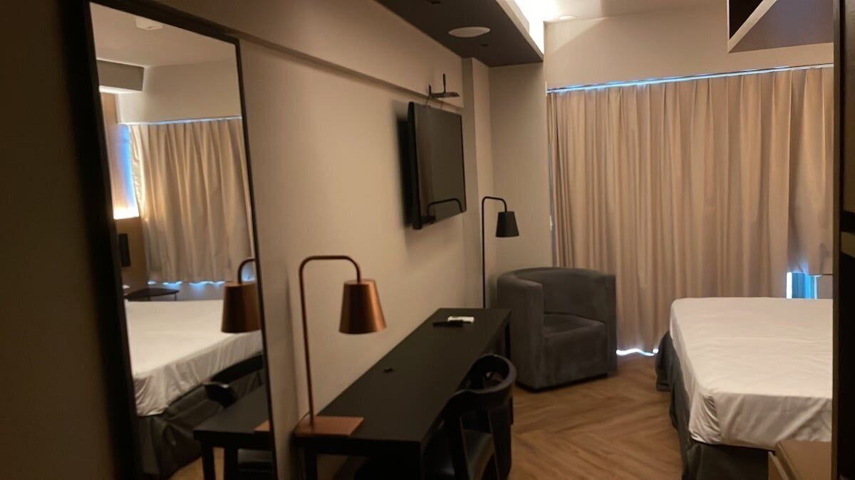 Habitación de hotel con cama, escritorio, silla, televisor y ventana con cortinas.