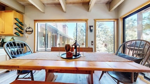 Uma sala de jantar com uma mesa de madeira, cadeiras e vista para um edifício através de grandes janelas.