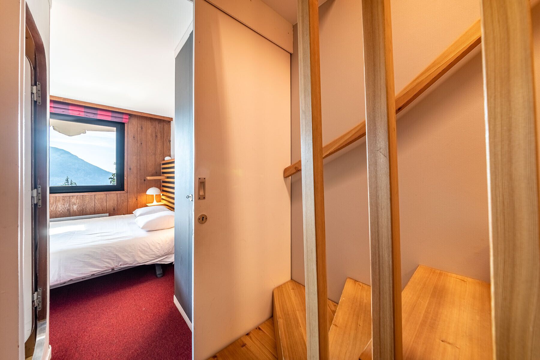Ein Schlafzimmer mit einem Bett, einem Fenster mit Bergblick und einer Holztreppe.