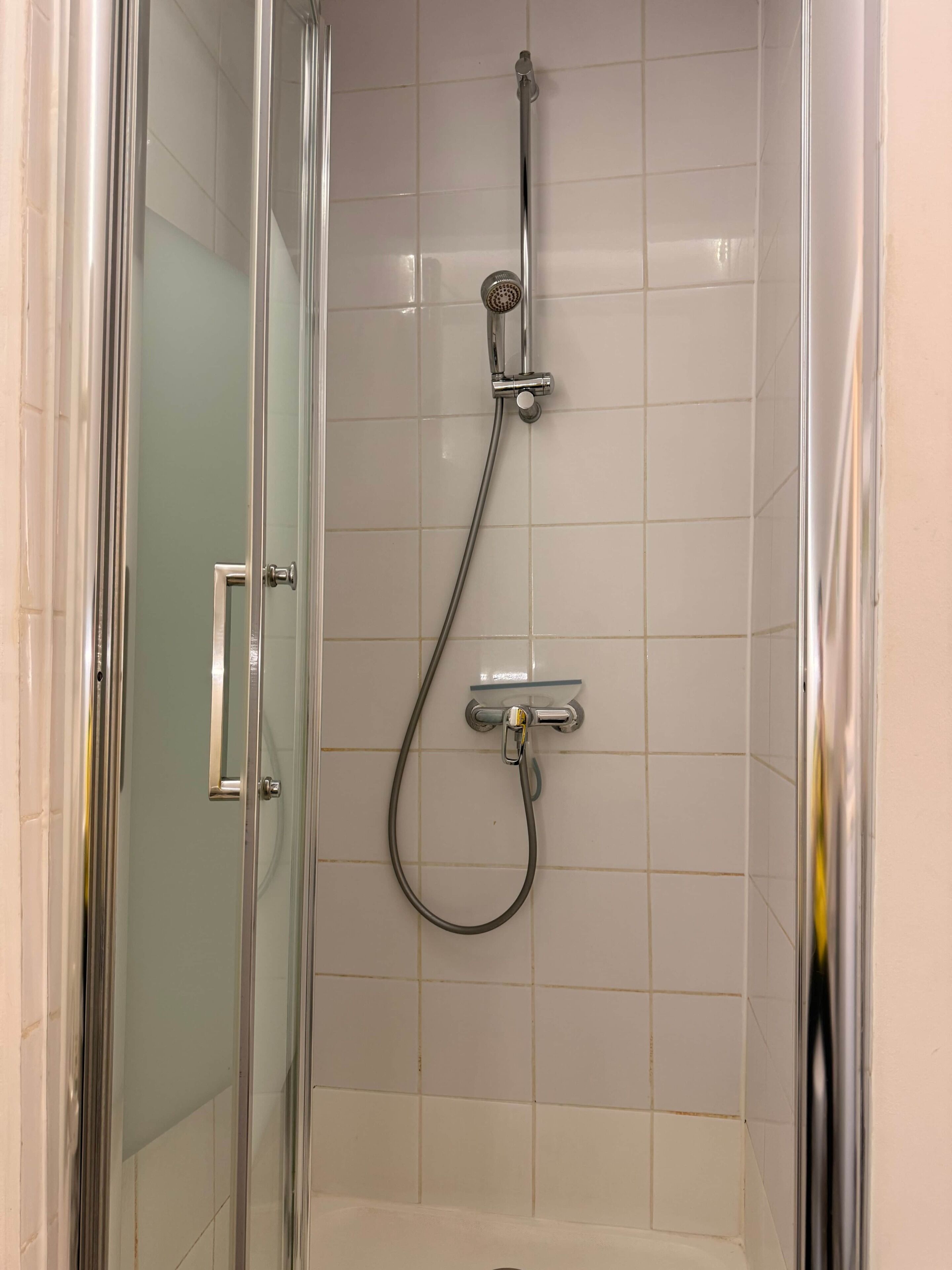 A glass-enclosed shower stall with a handheld showerhead and a wall-mounted faucet.