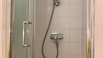 A glass-enclosed shower stall with a handheld showerhead and a wall-mounted faucet.