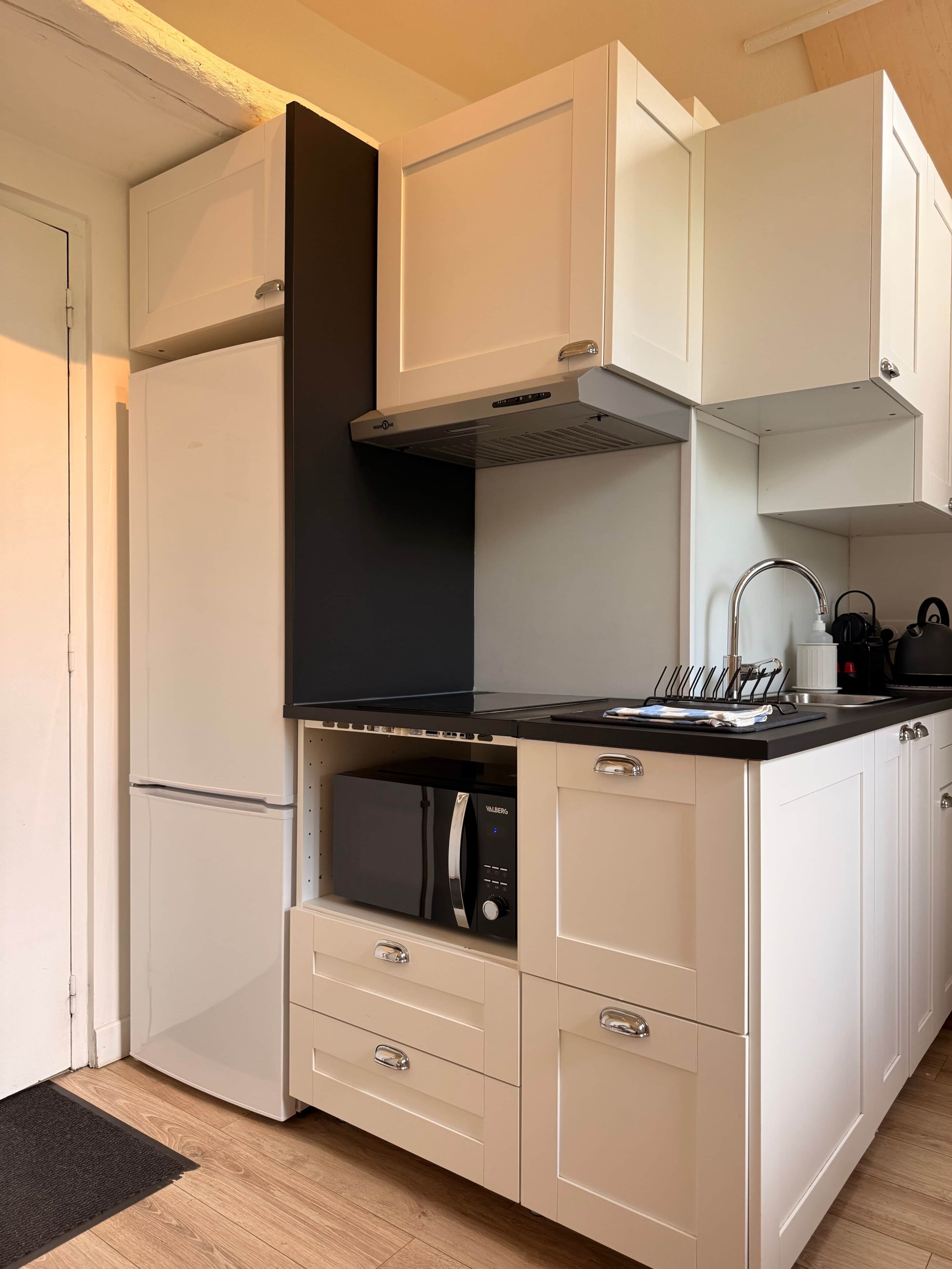 A modern kitchen with white cabinetry, a black range hood, a built-in microwave, and a stainless steel sink.