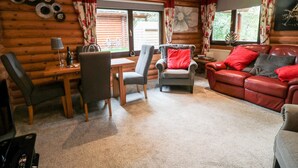 A cozy log cabin interior with a wooden dining table, two armchairs, a sofa, and a fireplace. - 10 Water's Edge (Morpeth)