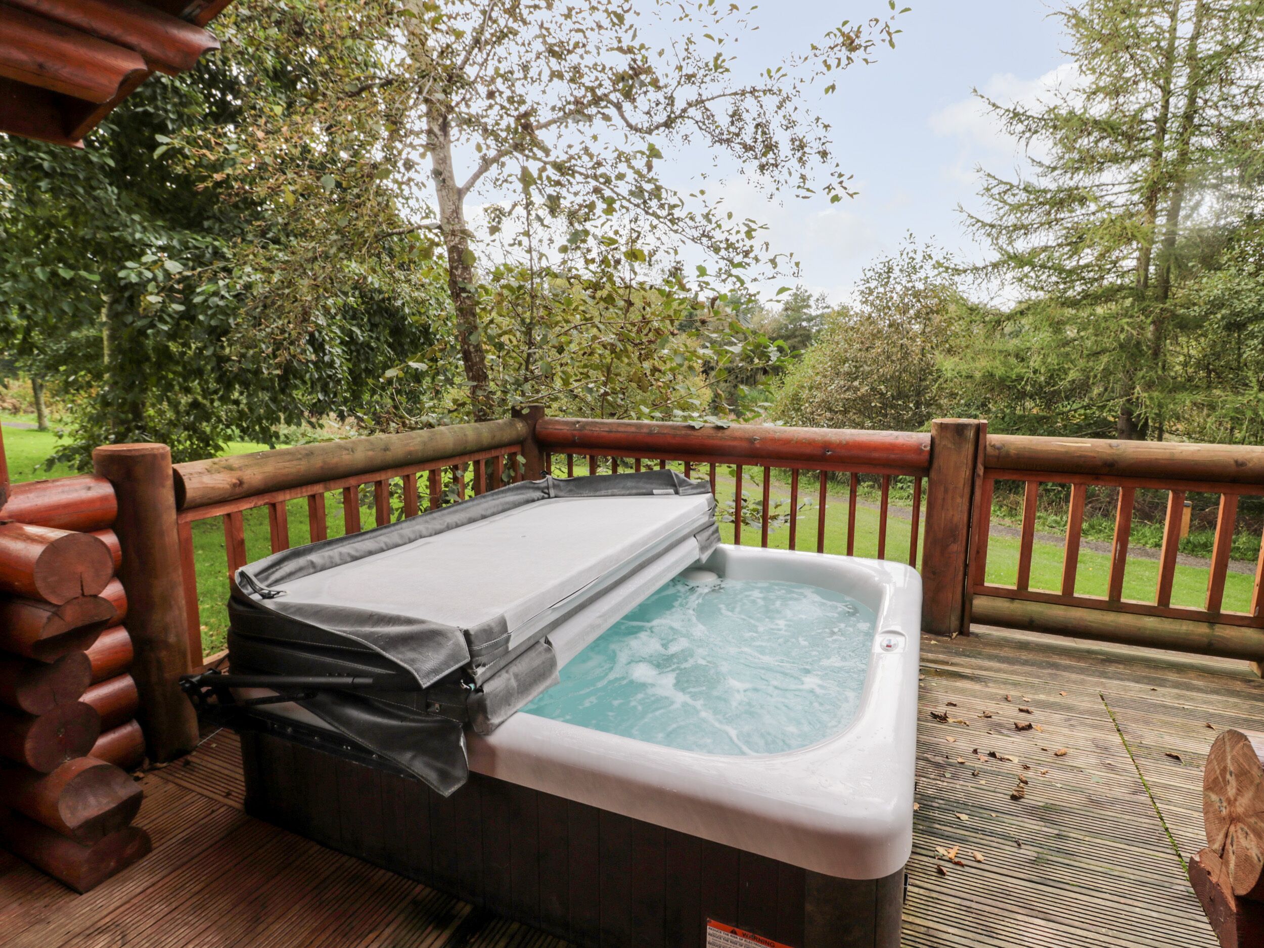 A hot tub on an outdoor deck with a wooden railing and logs.