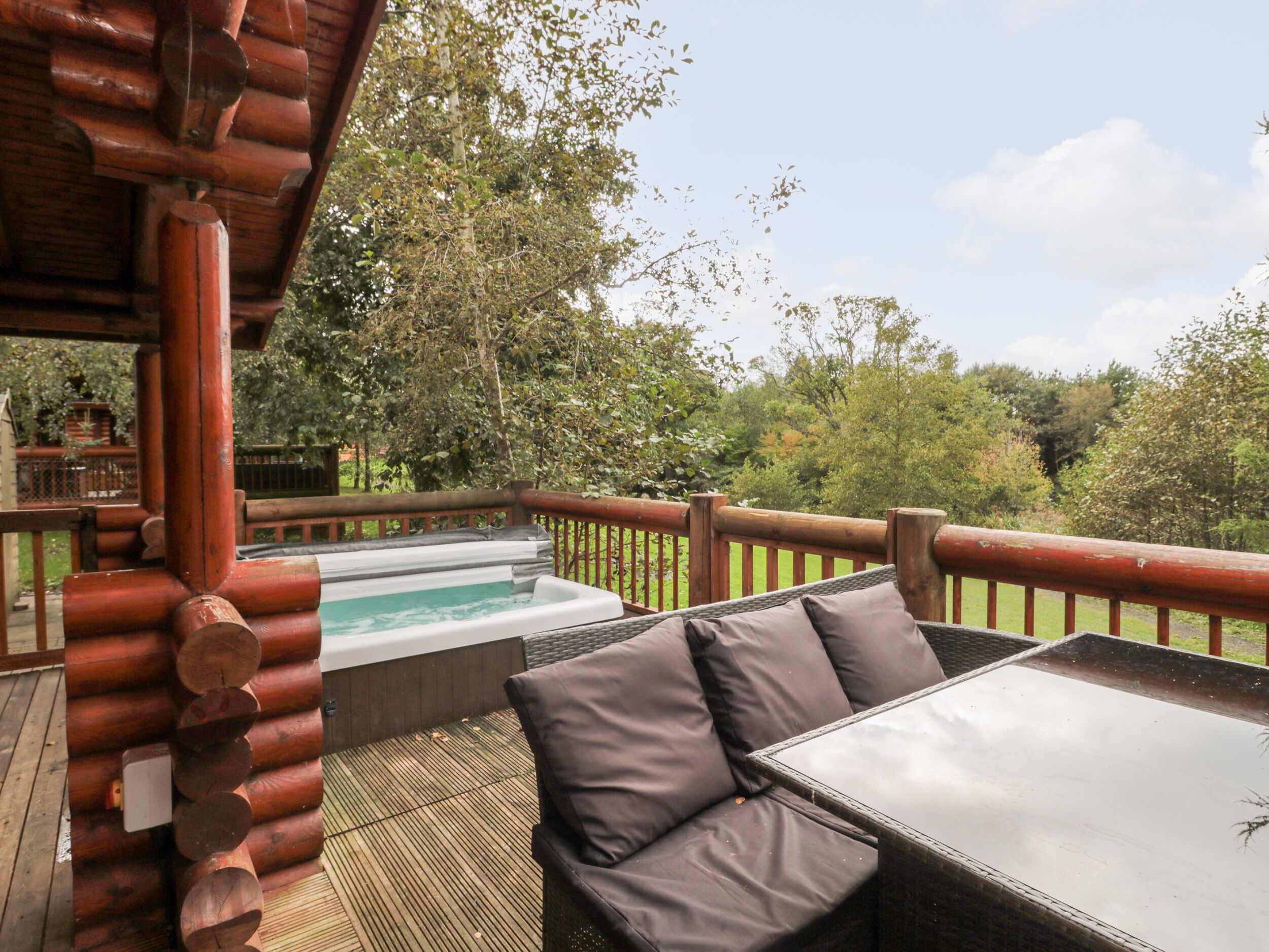 A wooden deck with a hot tub, outdoor seating, and a view of trees.