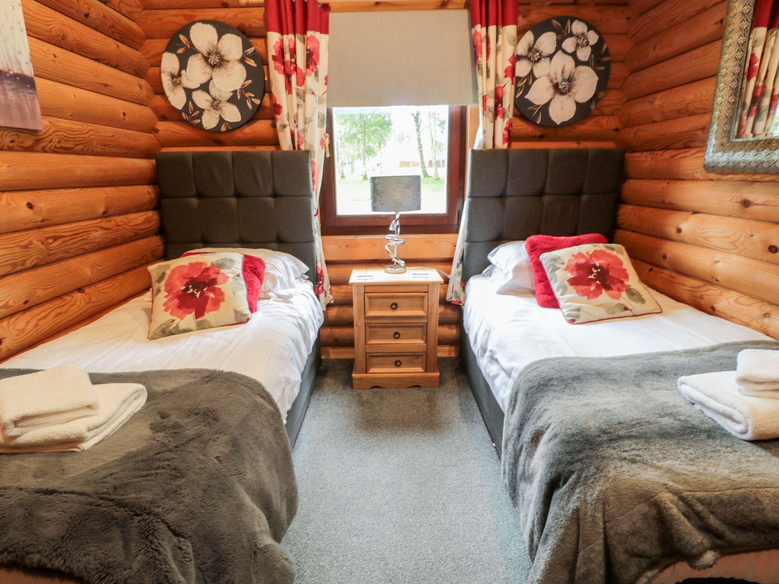 A cozy log cabin bedroom with two beds, a nightstand, and a window.