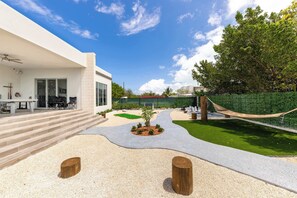 Un espace extérieur moderne avec des marches menant à un coin salon abrité, un petit jardin et un hamac.
