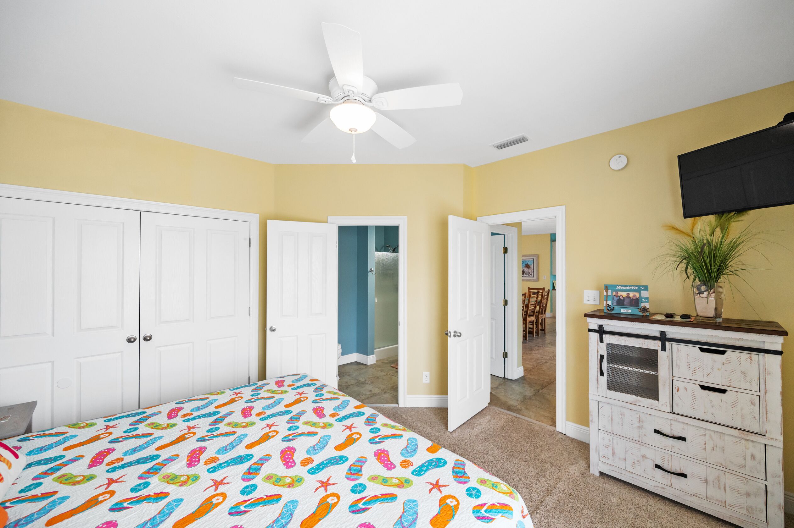 A bedroom with a bed, a ceiling fan, a dresser, and a television on the wall.
