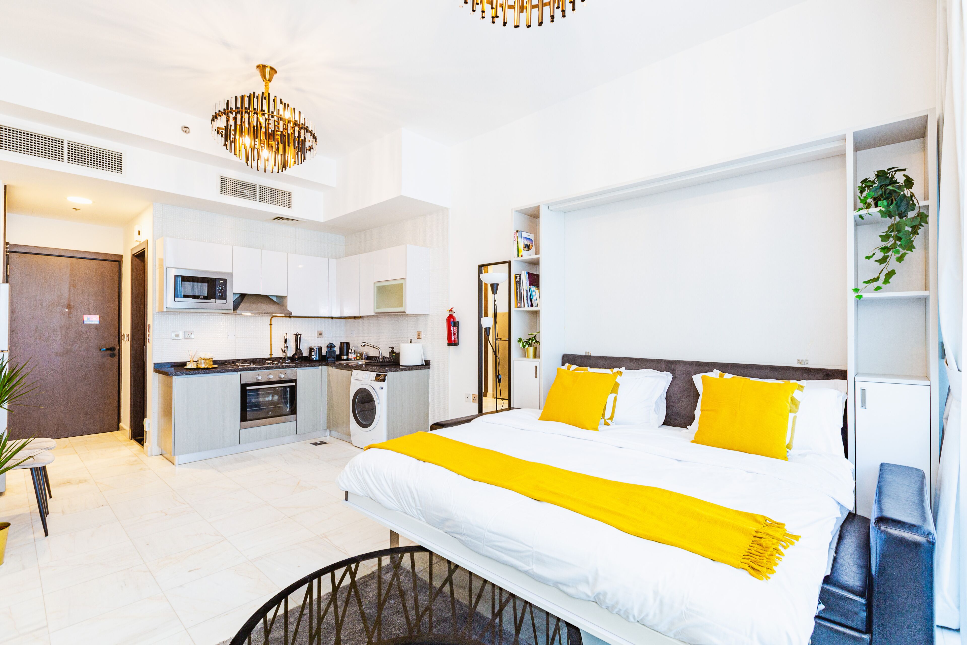 A modern hotel room with a large bed, a kitchenette, and a dining area.