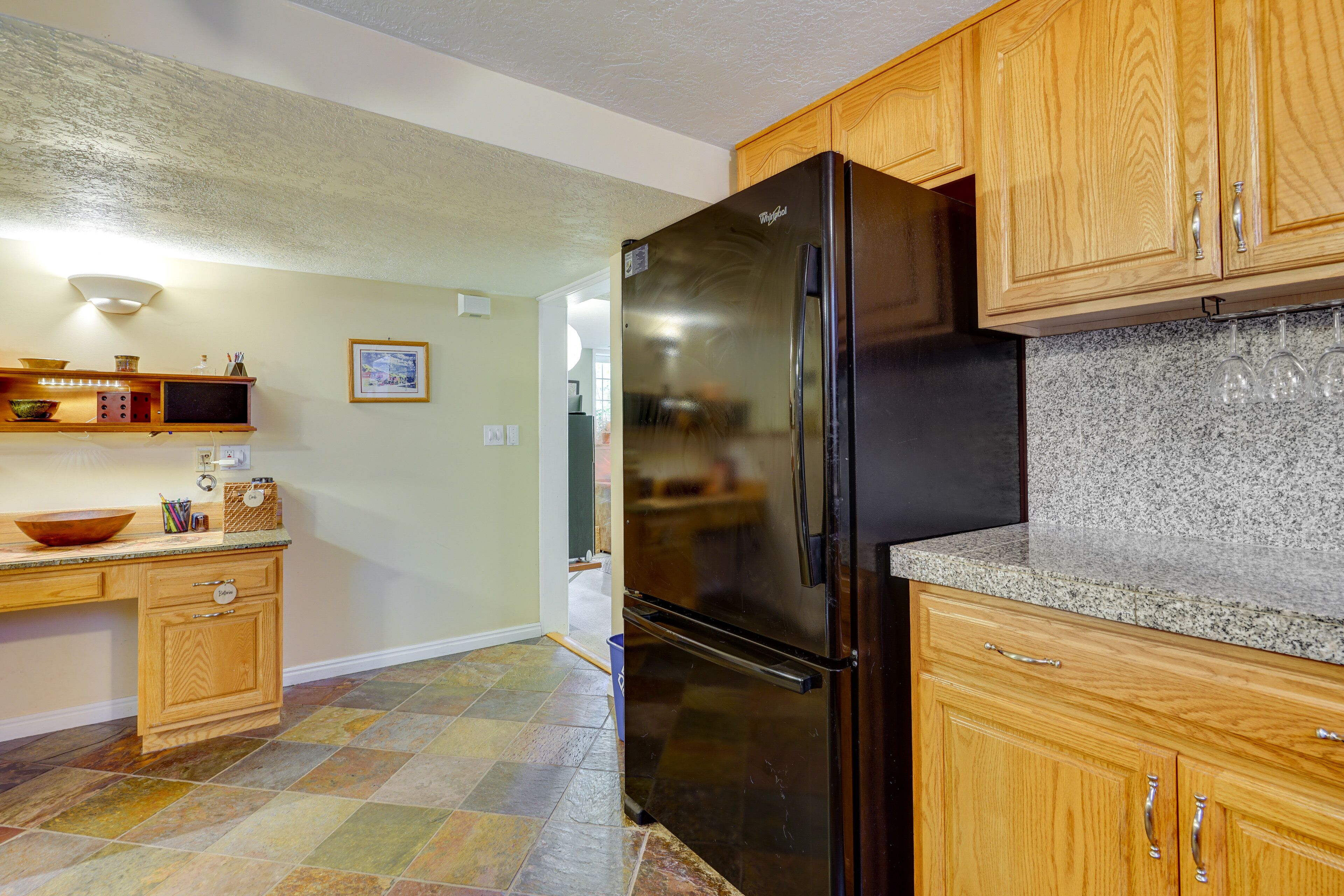 A kitchen with wooden cabinets, a black refrigerator, granite countertops, and a tiled floor.