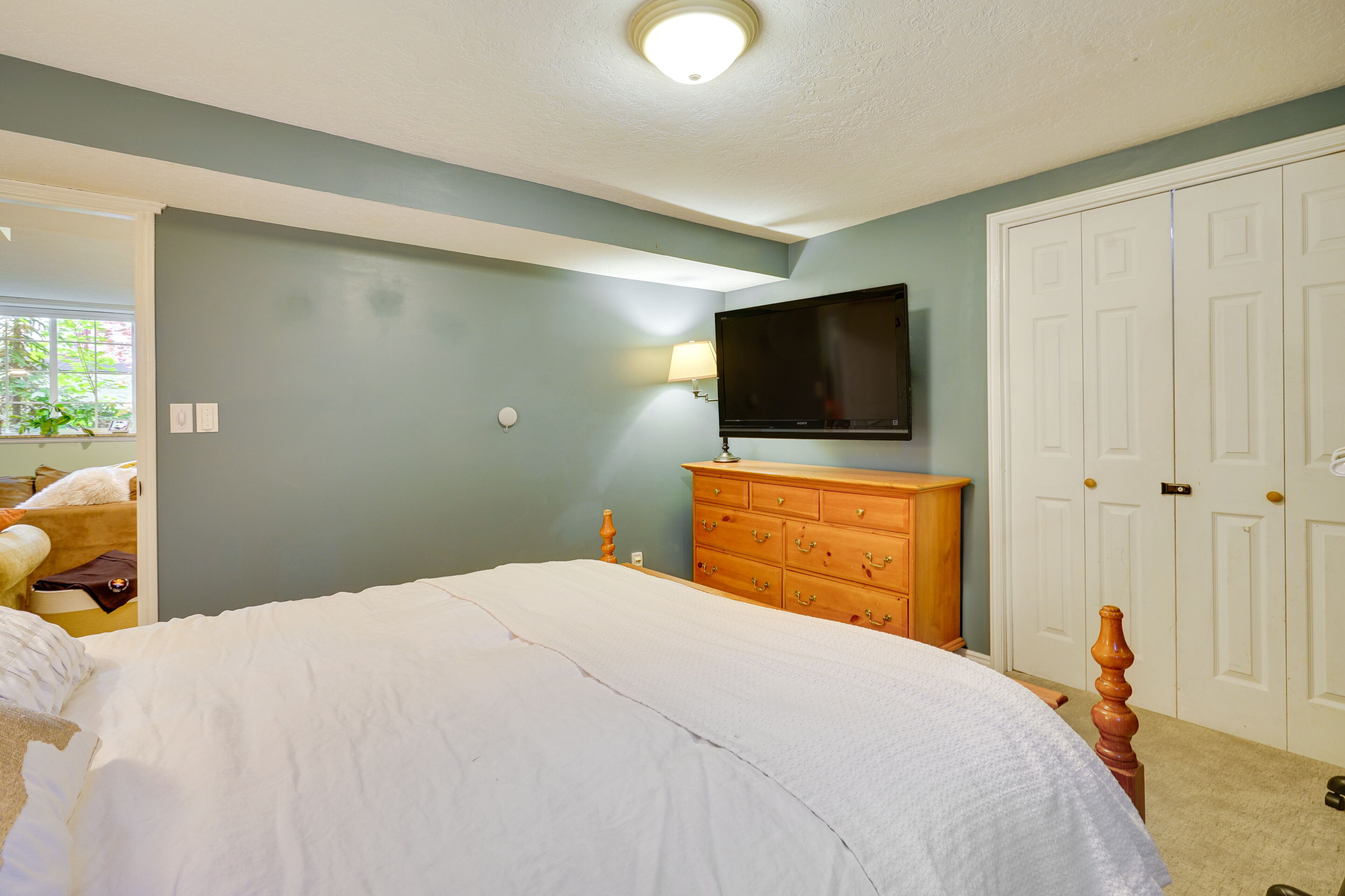 A bedroom with a large bed, a dresser, a television mounted on the wall, and a closet with double doors.
