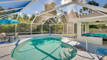 An indoor swimming pool with clear water, surrounded by a glass enclosure, and equipped with lounge chairs and a ceiling fan.