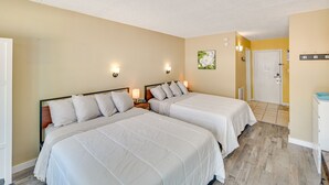 A hotel room with two beds, a wooden floor, a white door, and a small bathroom area.