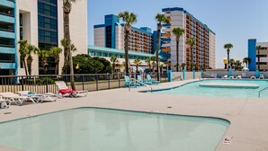 A hotel pool area with multiple pools, lounge chairs, and palm trees.