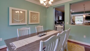 A dining area with a wooden table, white chairs, a chandelier, and nautical-themed wall art. - 6 Mi to Rehoboth Beach: Townhome w/ Pool Access! (Rehoboth Beach)