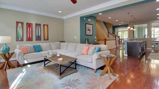 A spacious living room with a large sofa, a coffee table, and a ceiling fan. There is a staircase leading to an upper level, and a kitchen area is visible in the background. - 6 Mi to Rehoboth Beach: Townhome w/ Pool Access! (Rehoboth Beach)
