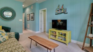 A living room with teal walls, a wooden bench, a yellow entertainment unit, and a TV. - 6 Mi to Rehoboth Beach: Townhome w/ Pool Access! (Rehoboth Beach)