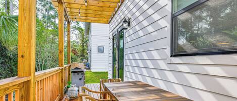 A wooden deck with a table and chairs, a barbecue grill, and a house with white siding and a green door.