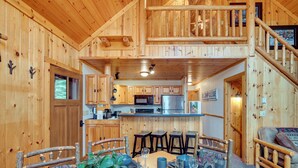 A wooden cabin interior with a dining area, kitchen, and a loft bedroom. - Lakefront Presque Isle Cabin w/ Private Dock (Presque Isle)