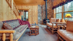 A cozy cabin interior with a wooden interior, stone walls, a fireplace, and a large window. - Lakefront Presque Isle Cabin w/ Private Dock (Presque Isle)