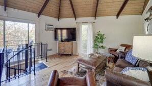 Un salon spacieux doté d’un plafond en bois, d’un téléviseur à écran plat, de meubles en cuir et d’un balcon avec coin salon extérieur.